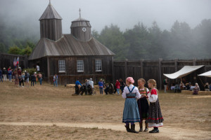 Three girls in traditional russian attire in front of Russian Orthodox Chapel